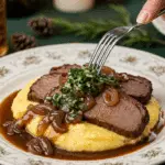 A beautiful plate of a homemade, elegant, and sliced Braised Brisket, being served over creamy polenta with a green gremolata at a holiday dinner.